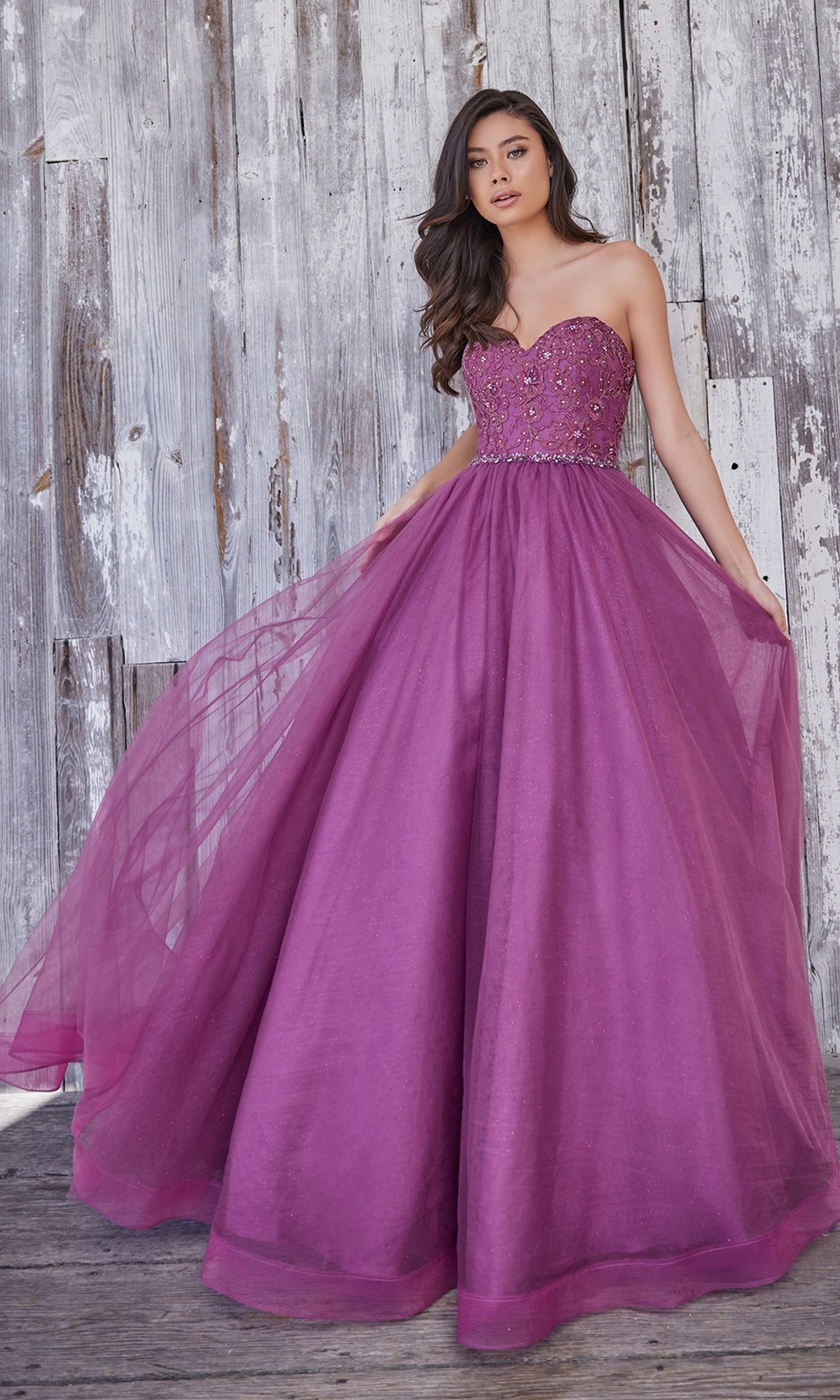 Wearing the Colette Strapless Sweetheart Prom Ball Gown CL5193, a woman poses in front of a weathered wooden wall, showcasing the floor-length purple tulle skirt and elegant silhouette.